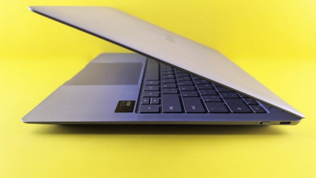 Partly open silver laptop photographed from the side against a bright yellow background.