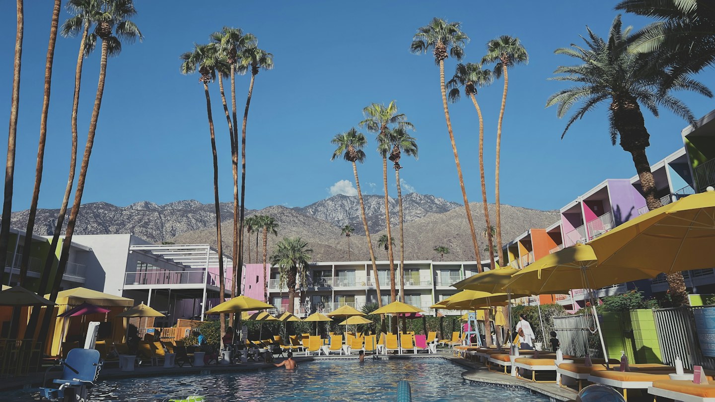 Swimming pool, yellow umbrellas, and colorful hotel balconies beneath palm trees at The Saguaro in Palm Springs.